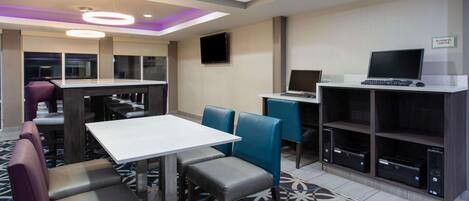 A modern hotel room with a dining area, a business center, and a flat-screen TV.