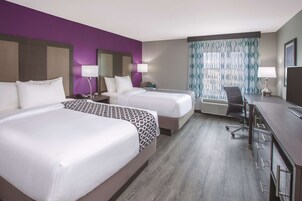 A hotel room with two beds, a desk, a chair, and a large window with patterned curtains.