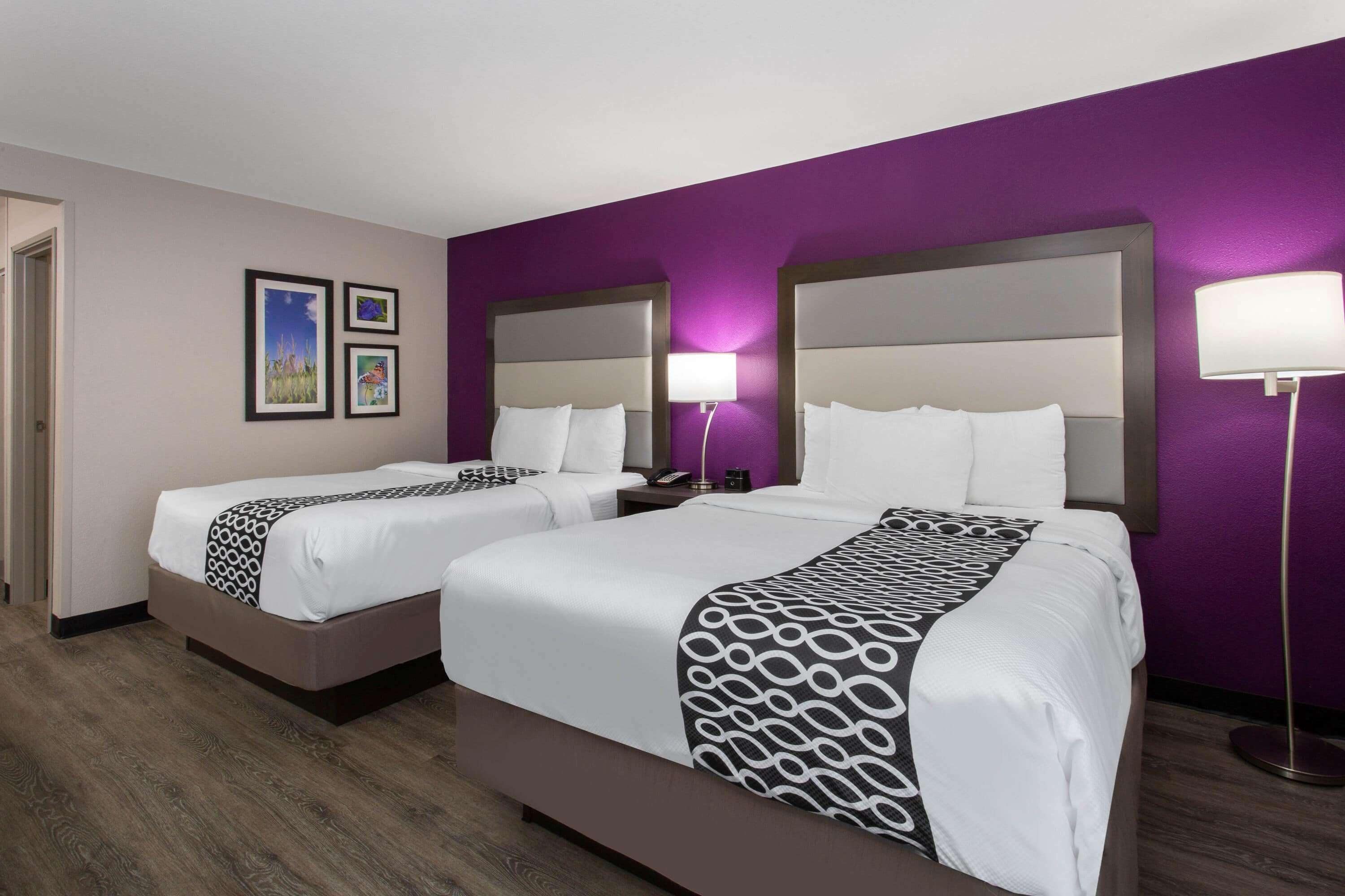 A hotel room with two beds, a purple wall, and a wooden floor.