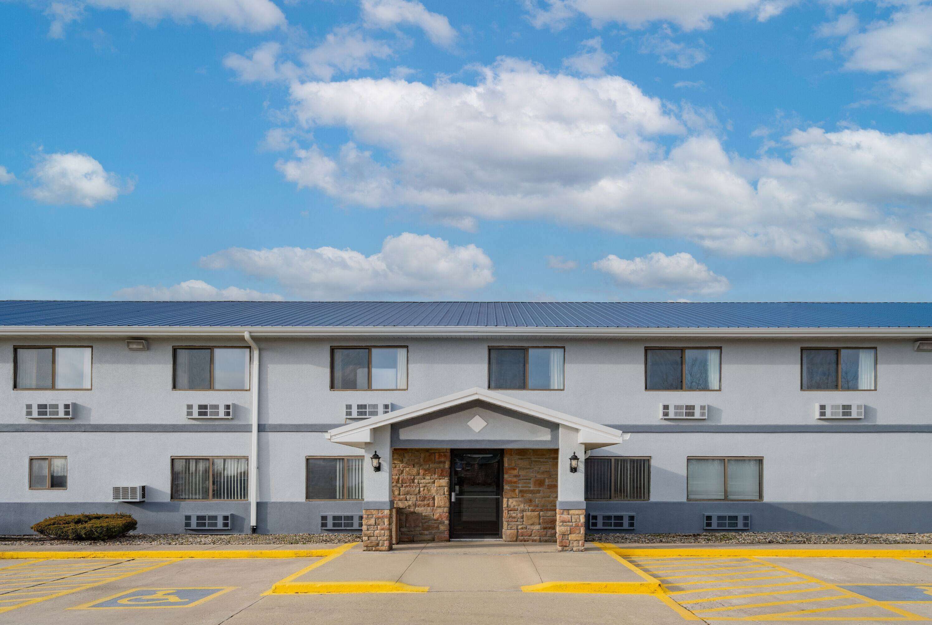A multi-story hotel with a flat roof, a central entrance with a stone facade, and a parking lot with handicapped accessibility.