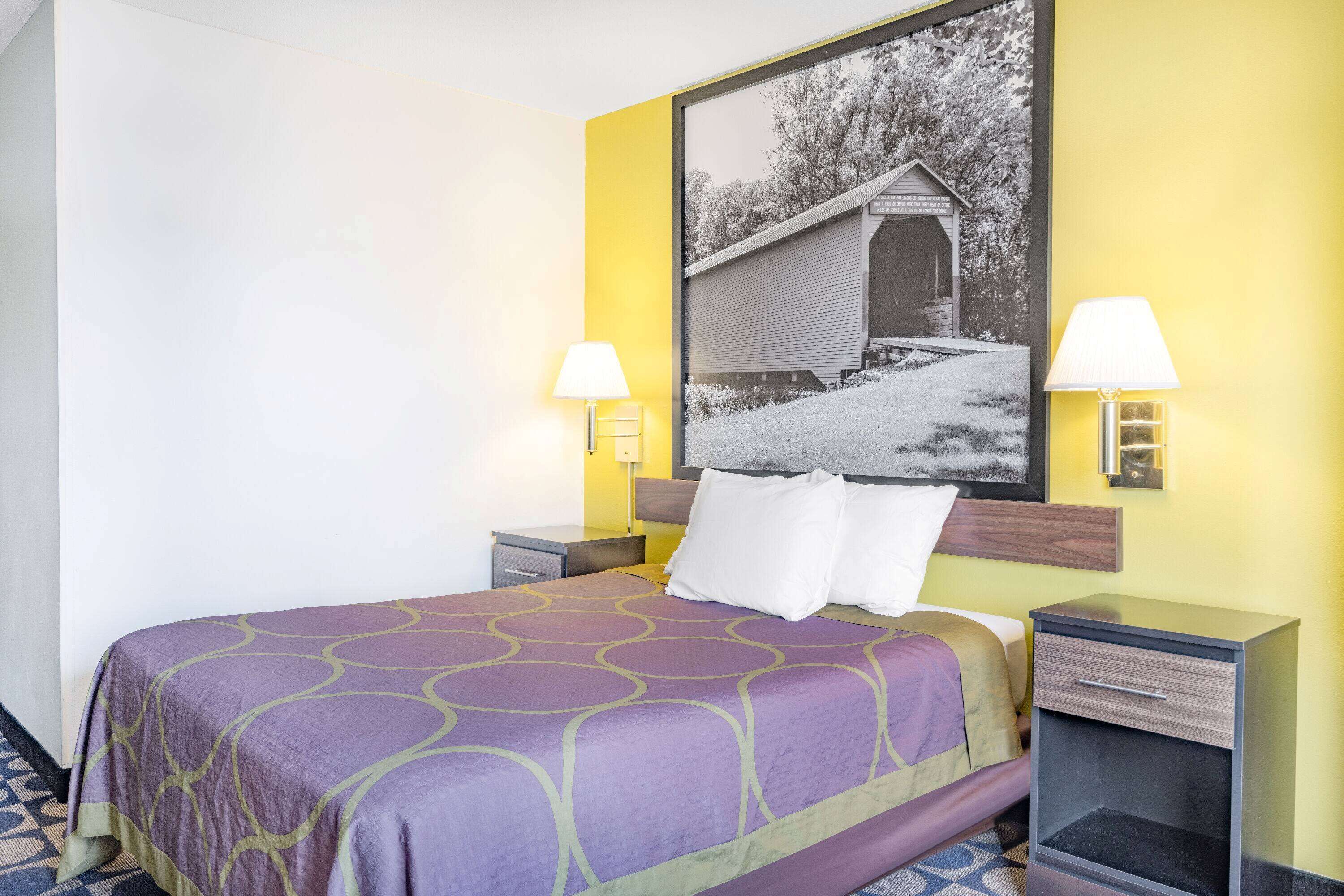 Une chambre d’hôtel comprenant un lit, deux tables de chevet, une petite table et une lampe fixée au mur.