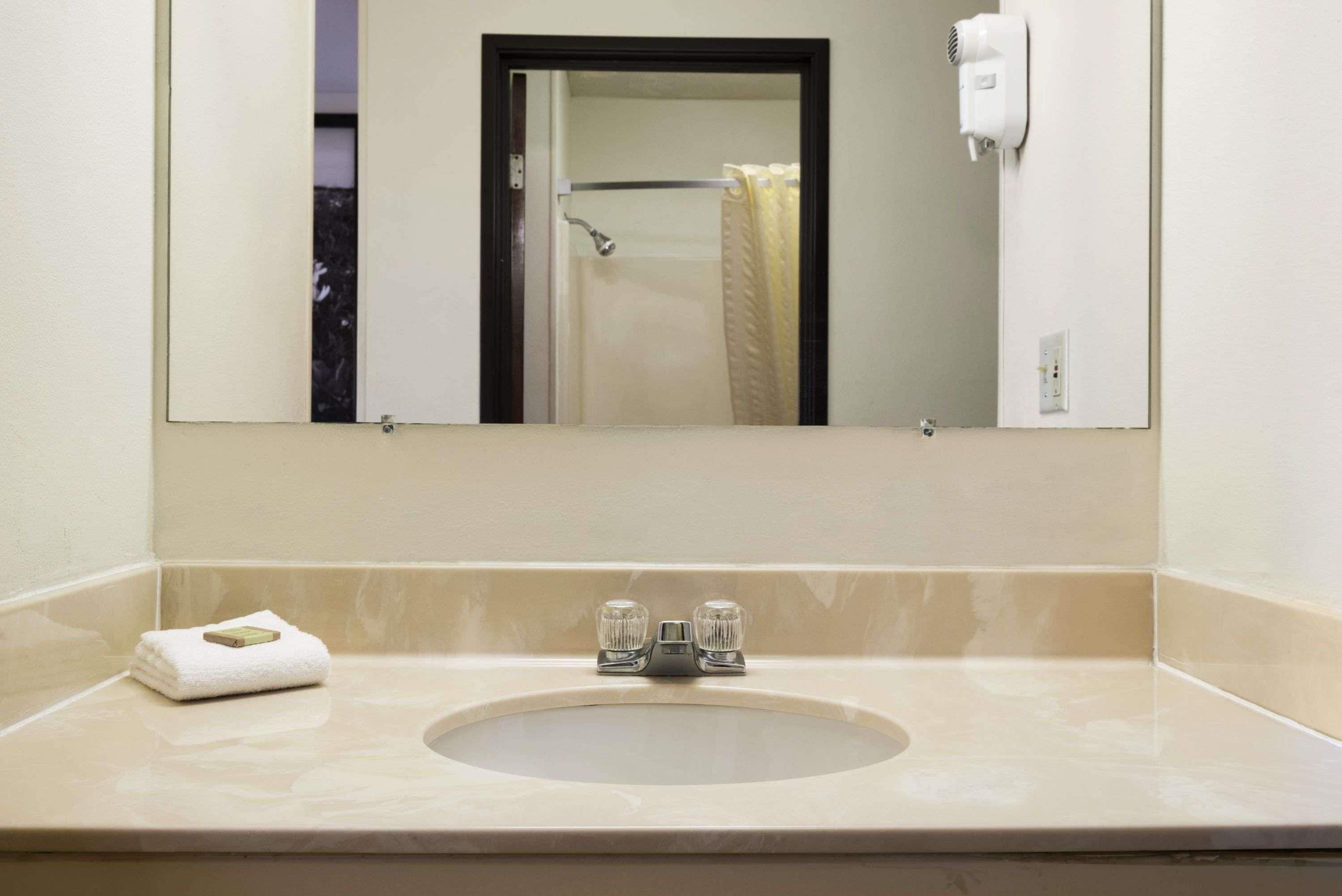 Un baño con lavabo, espejo, toalla y secador de pelo fijado a la pared.