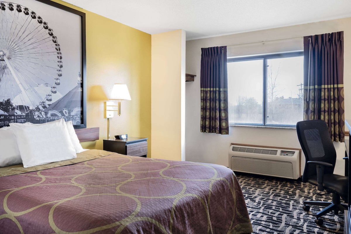 Habitación de hotel con una cama grande, un escritorio, una silla, un ventanal con cortinas, un calentador de pared y un cartel grande de una noria.