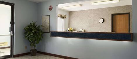 A reception area with a reception desk, a potted plant, a clock, and an exit sign.