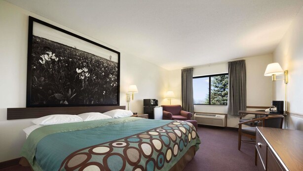 Ein Hotelzimmer mit einem großen Bett, einem Schreibtisch, einem Stuhl, einem Fernseher und einem Fenster mit Vorhängen.