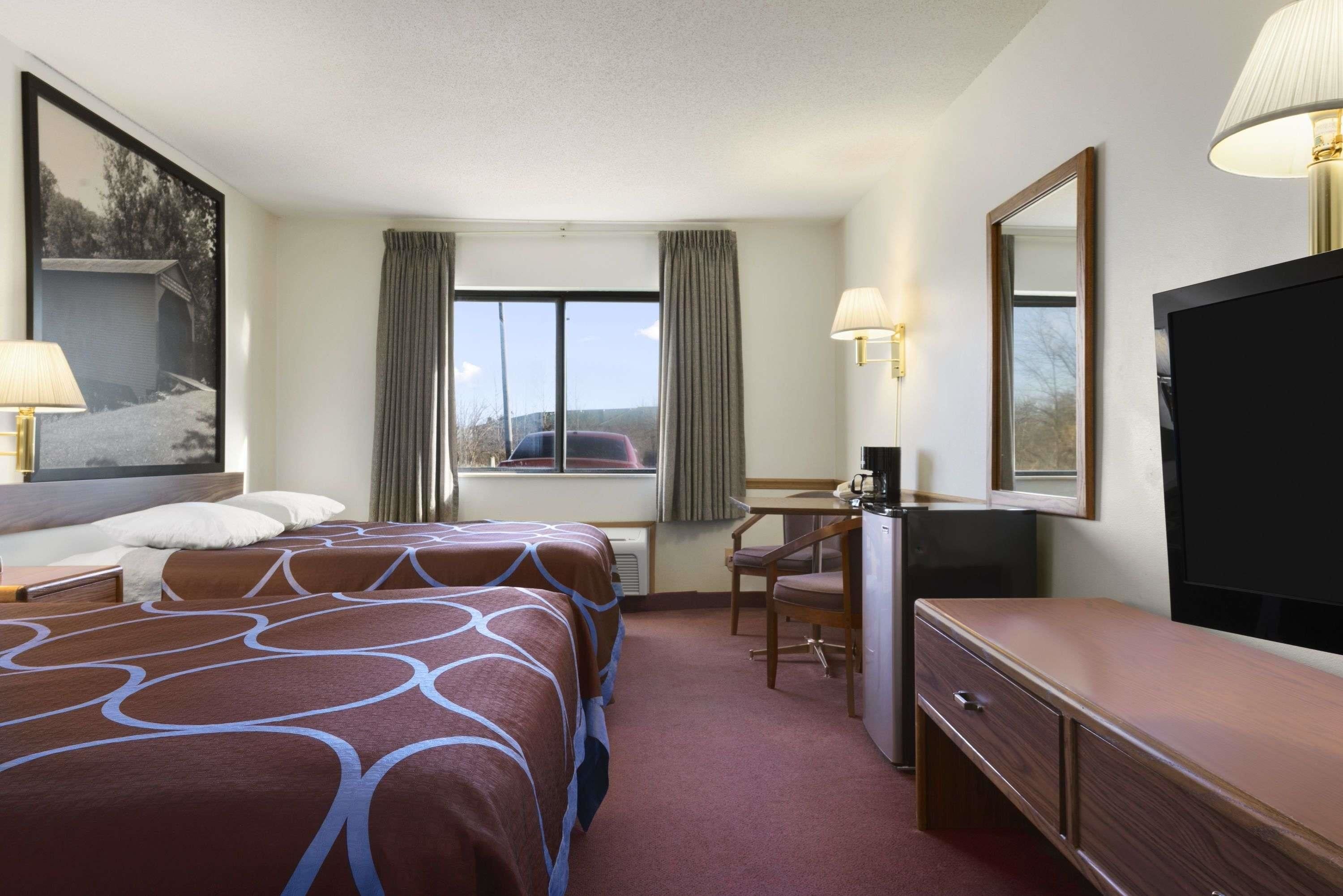 A hotel room with two beds, a desk, a dresser, a TV, and a window with curtains.