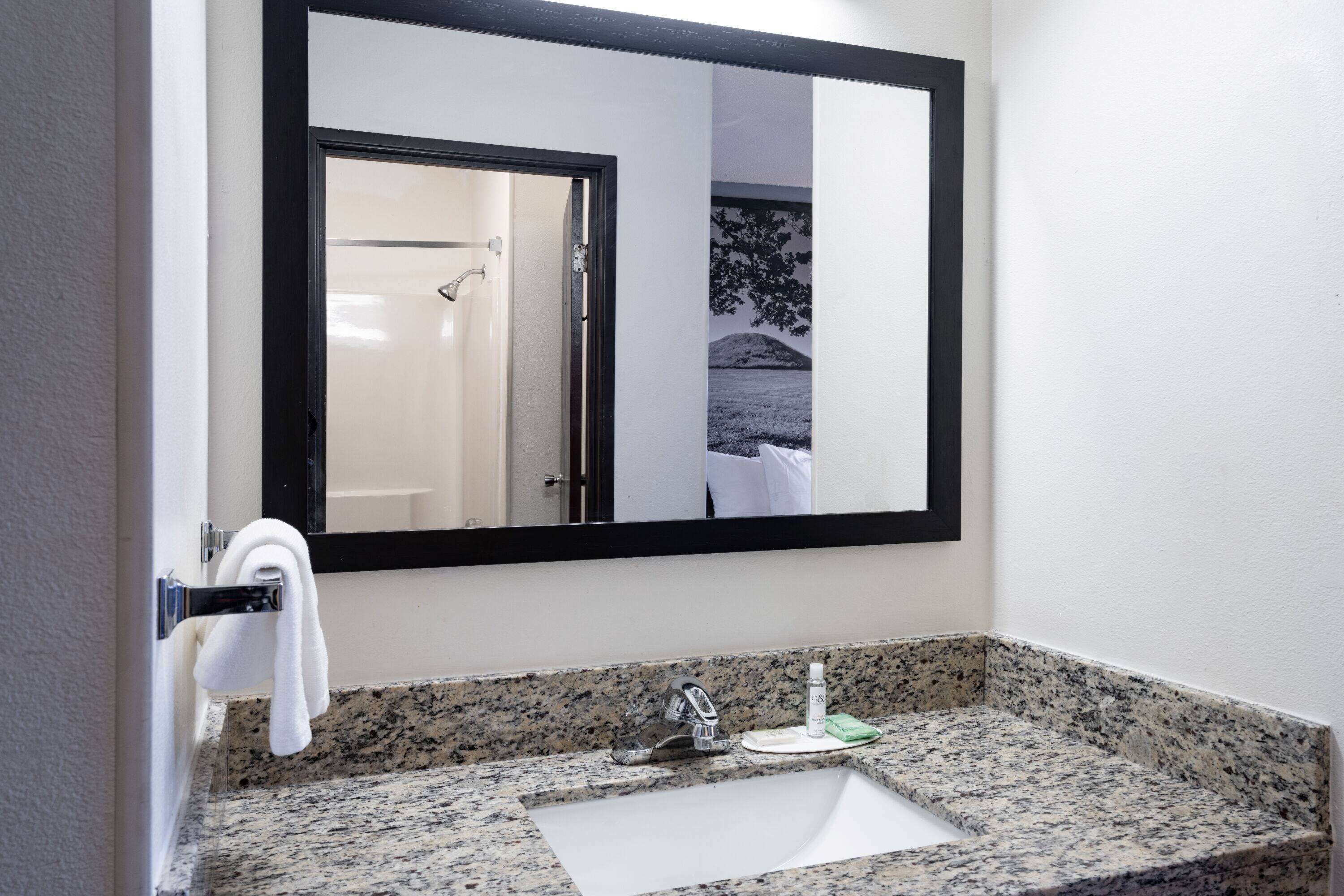 A bathroom with a granite countertop, a white sink, a mirror, and a towel hanging on a rack.