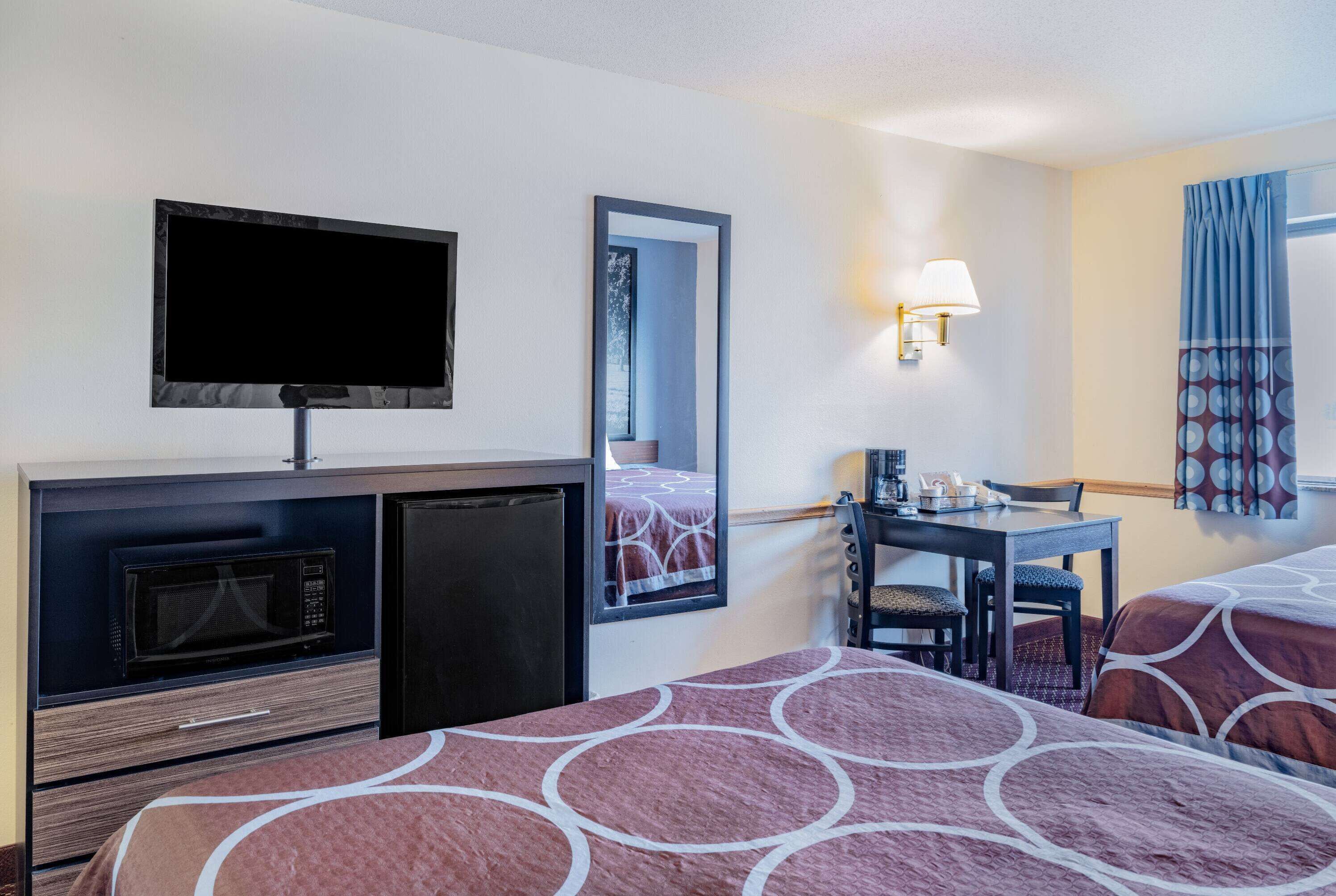 A hotel room with a TV, microwave, small fridge, a desk with a chair, and two beds with patterned bedding.