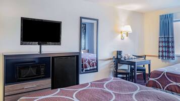 A hotel room with a TV, microwave, small fridge, a desk with a chair, and two beds with patterned bedding.