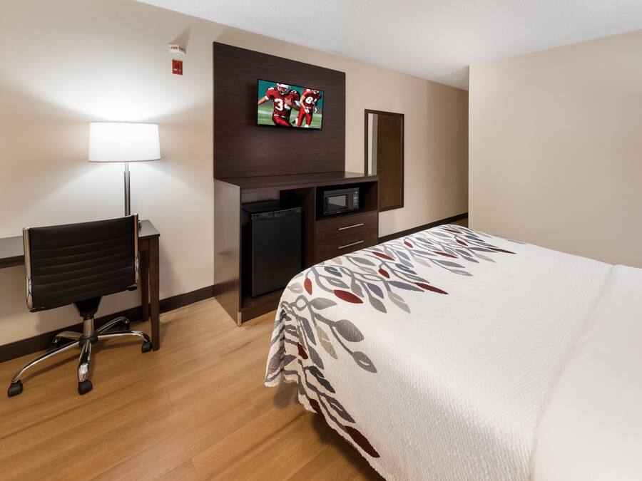 A hotel room with a bed, a desk, a chair, a television, and a microwave.