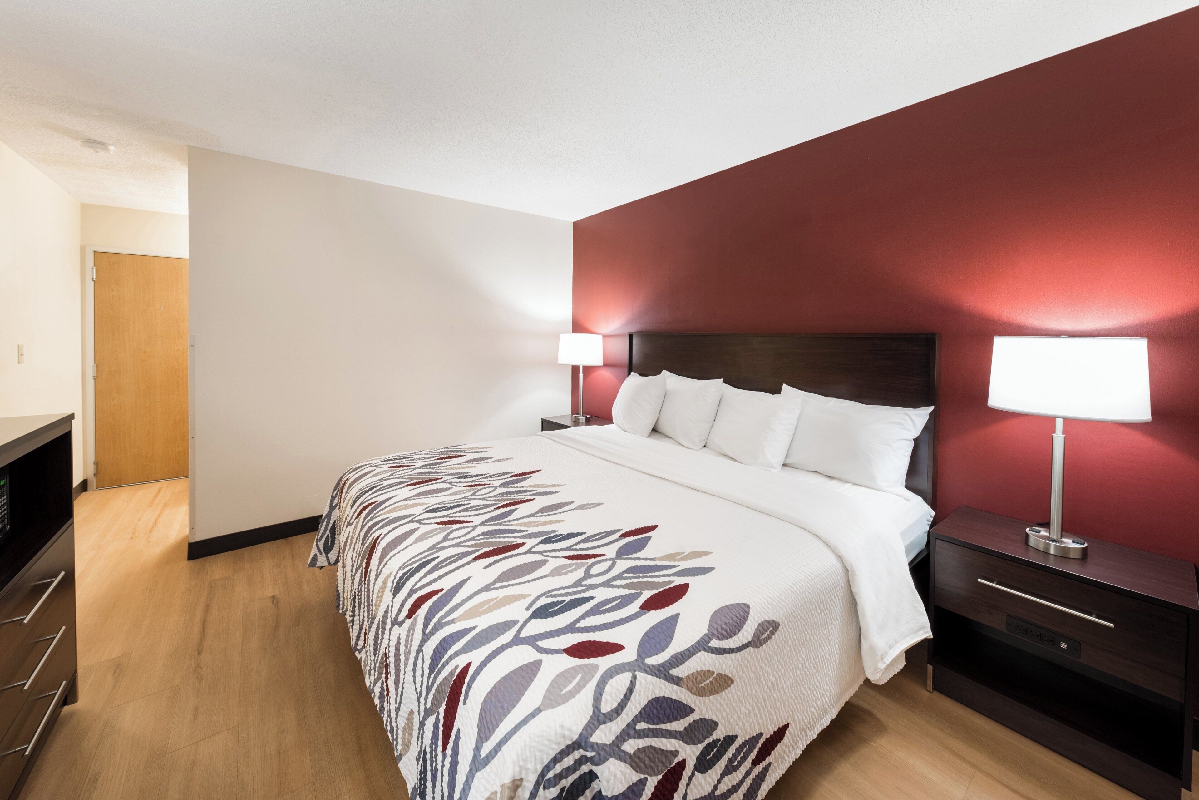 Een hotelkamer met een bed, nachtkastje, lamp en een houten garderobe.