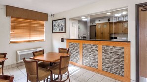A dining area with a wooden table and chairs, a kitchen visible through a glass partition, and a framed picture on the wall. - Super 8 by Wyndham College Park Wash DC Area (College Park)