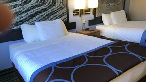 A hotel room with a large bed, two smaller beds, a nightstand with a lamp, and a wall with a textured design. - Boarders Inn & Suites by Cobblestone Hotels - Waterloo/Cedar Falls (Waterloo)