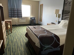 A hotel room with a bed, a desk, a chair, a TV, a lamp, and a window.