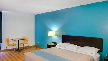 A hotel room with a bed, a desk, two chairs, and a nightstand with a lamp.
