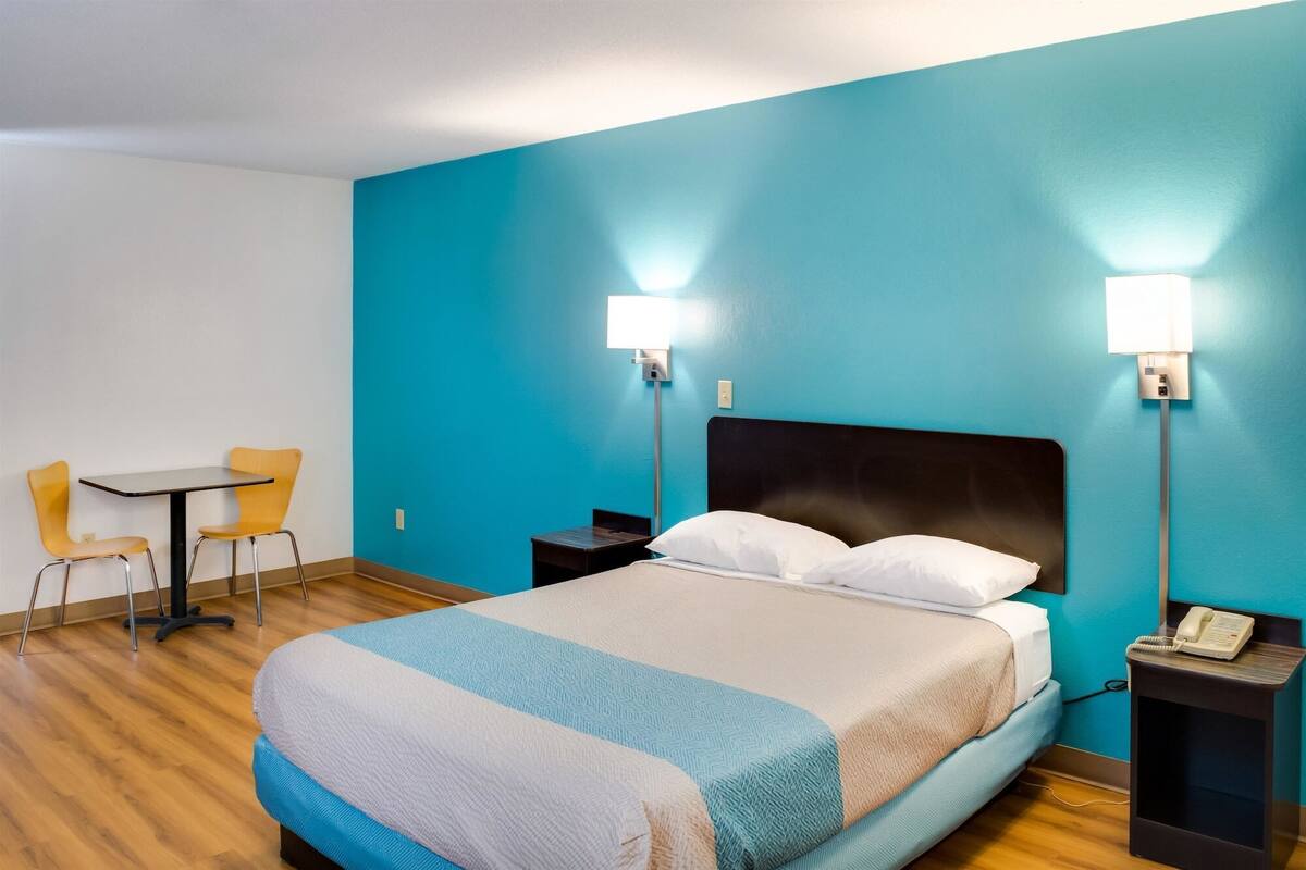 A hotel room with a bed, two bedside tables, a desk with a chair, and two wall-mounted lamps.