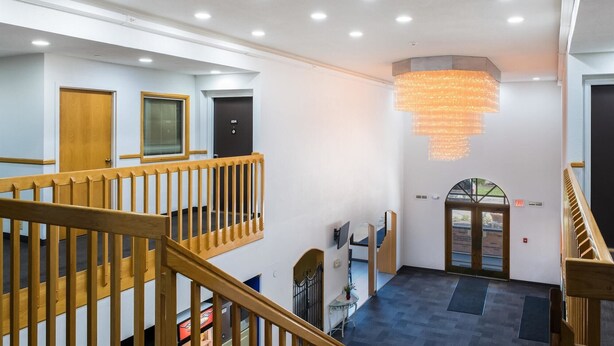 A spacious lobby with a wooden staircase, a chandelier, and a reception desk. - Motel 6 Richmond, IN (Richmond)