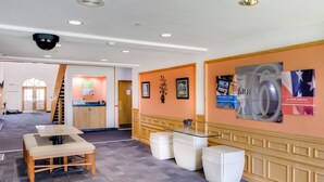 A hotel lobby with a reception desk, a staircase, and a seating area with a table and chairs. - Motel 6 Richmond, IN (Richmond)