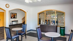 A hotel lobby with two round tables, four chairs, a bar area with a glass partition, a clock on the wall, and a staircase in the background. - Motel 6 Richmond, IN (Richmond)