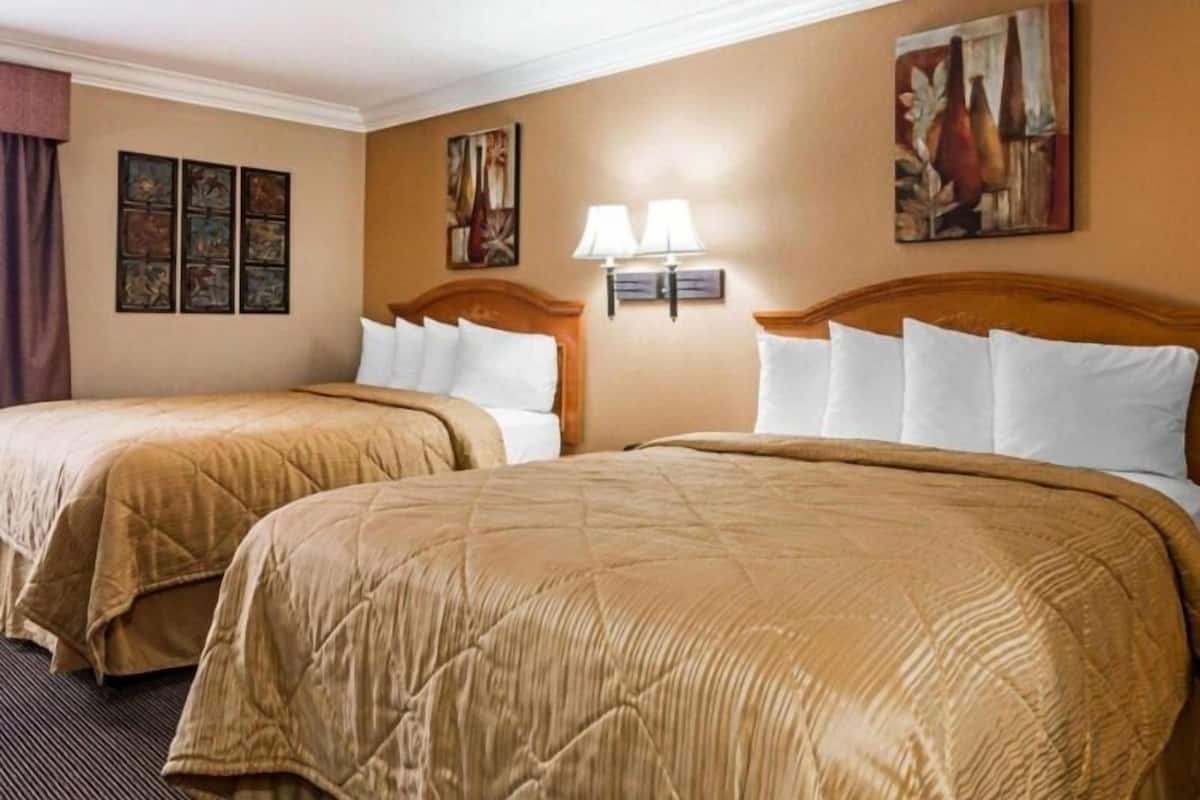 Quarto de hotel com duas camas, paredes bege e obras de arte.