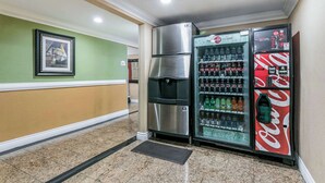 A hallway with a refrigerator, a vending machine, and a framed picture on the wall. - Quality Inn & Suites (College Park)