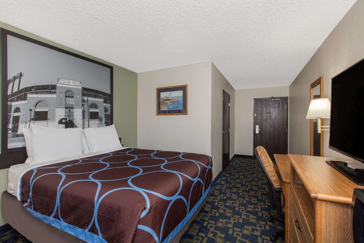 A hotel room with a bed, a desk, a TV, and a framed picture on the wall.