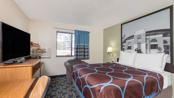 Una habitación de hotel con una cama grande, televisor, escritorio y ventana con cortinas.