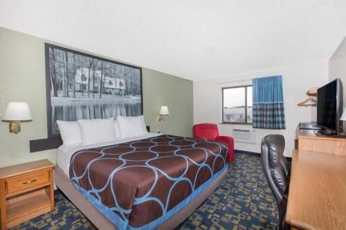A hotel room with a bed, a desk, a chair, a television, and a window.