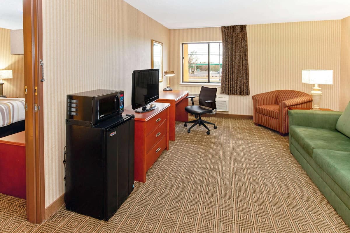 A hotel room with a bed, a desk with a television, a computer, a chair, a couch, and a window with curtains.