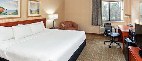 Habitación de hotel con una cama grande, un escritorio con computadora, una silla, un televisor y dos cuadros en la pared.