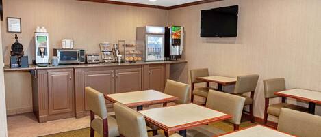 Una habitación de hotel con kitchenette, un televisor de pantalla plana y una zona de estar con mesas y sillas.