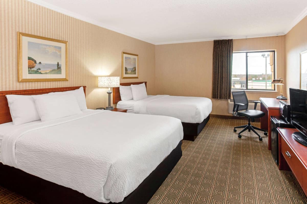 A hotel room with two beds, a desk with a chair, a television, and a window with a view.