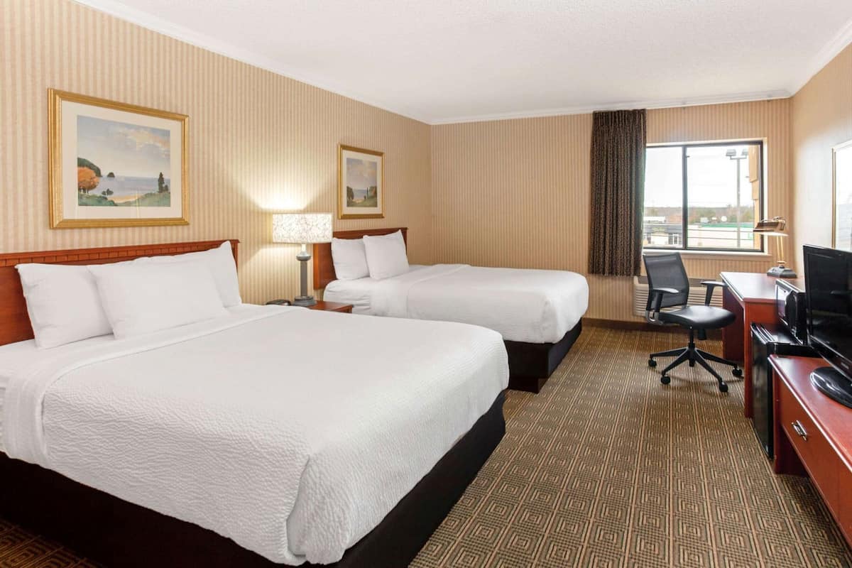 A hotel room with two beds, a desk, a chair, a television, and two framed pictures on the wall.
