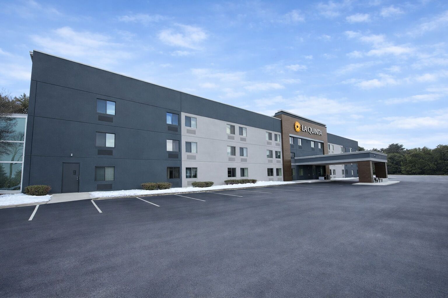 A modern hotel building with a flat roof, multiple windows, and a parking lot in front.