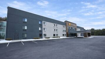 A modern hotel building with a flat roof, multiple windows, and a parking lot in front.