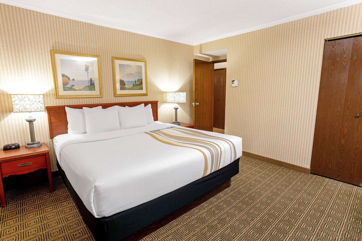 A hotel room with a large bed, two bedside tables with lamps, a wooden wardrobe, and two framed pictures on the wall.