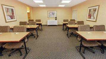 A conference room with a long table, multiple chairs, a white tablecloth, framed pictures on the walls, and carpeted flooring.