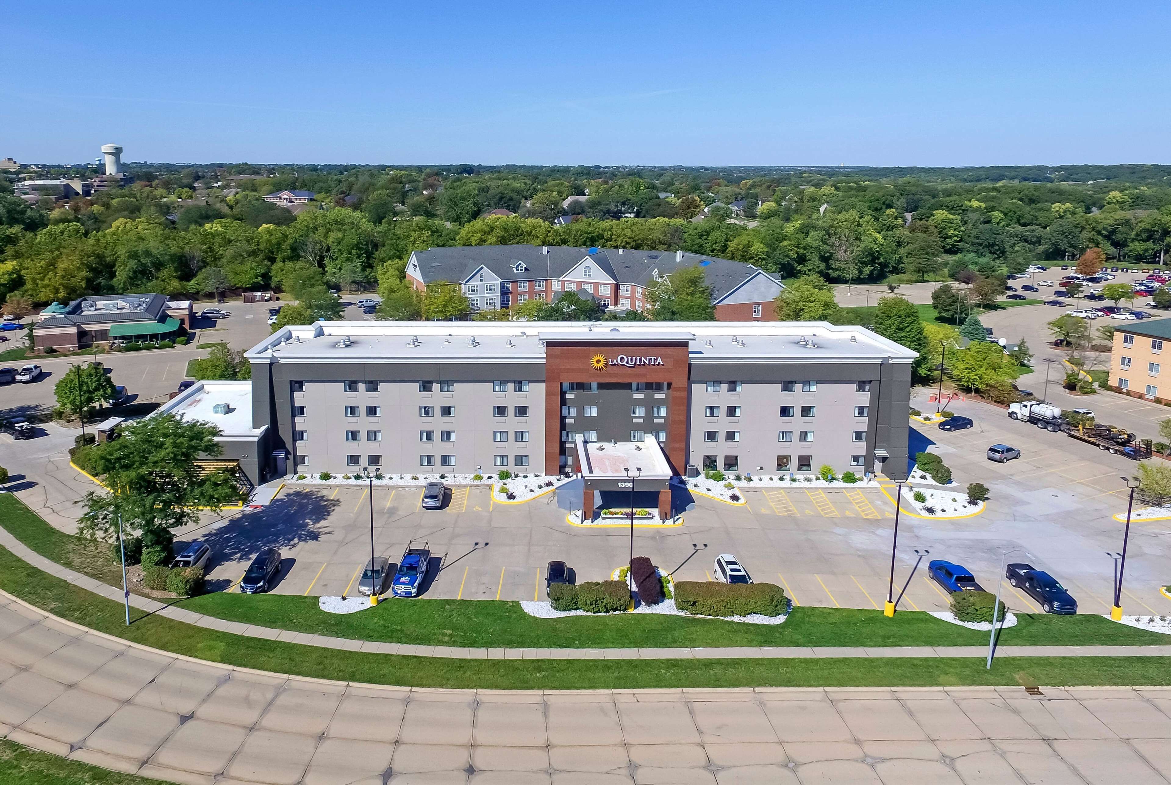 A hotel with a central entrance, parking lot, and surrounding greenery.