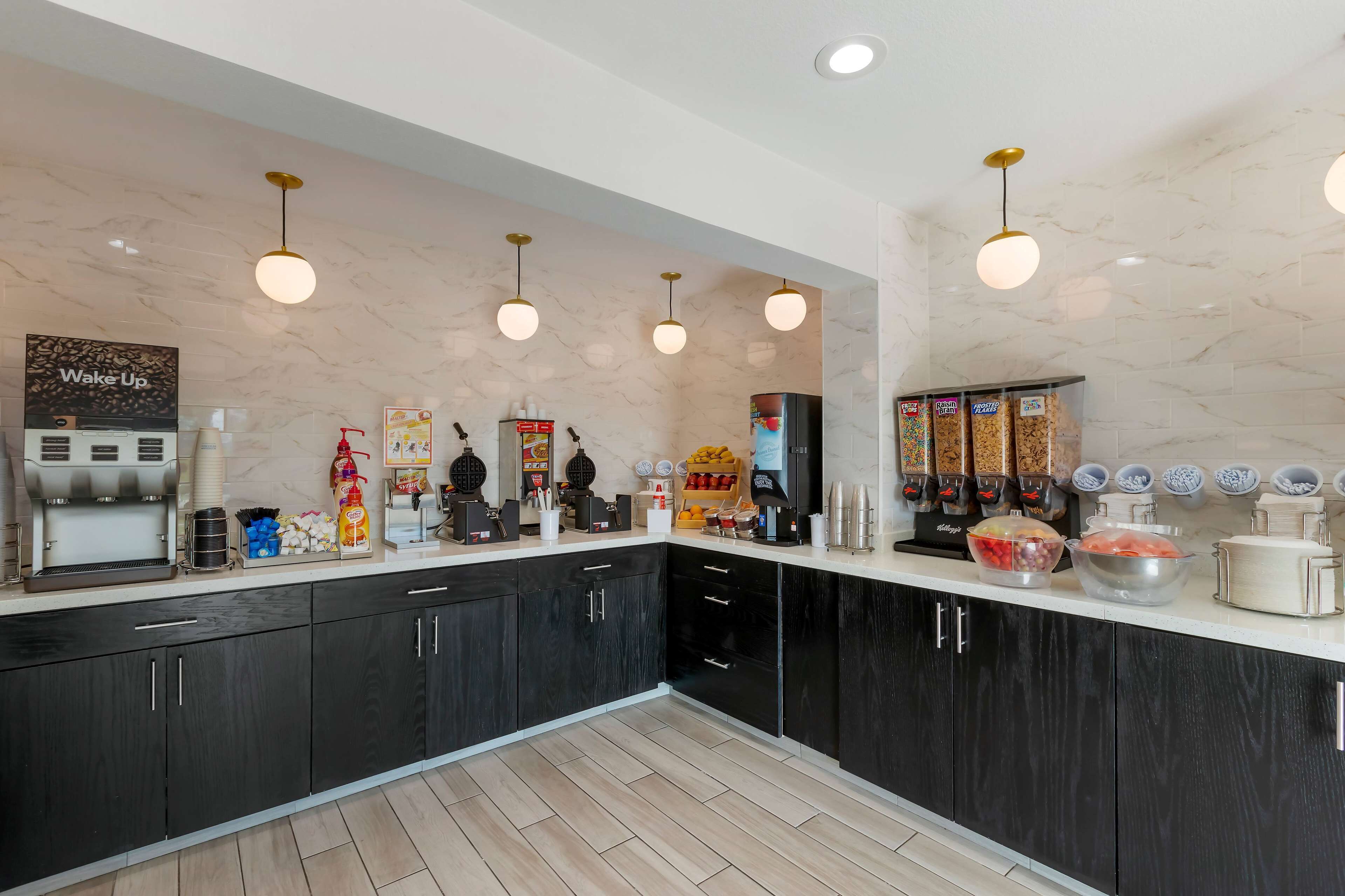 A modern kitchen with marble countertops, black cabinets, and various food and drink dispensers.
