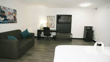 Habitación de hotel con cama, escritorio con computadora, una silla, televisor y obras de arte en las paredes.