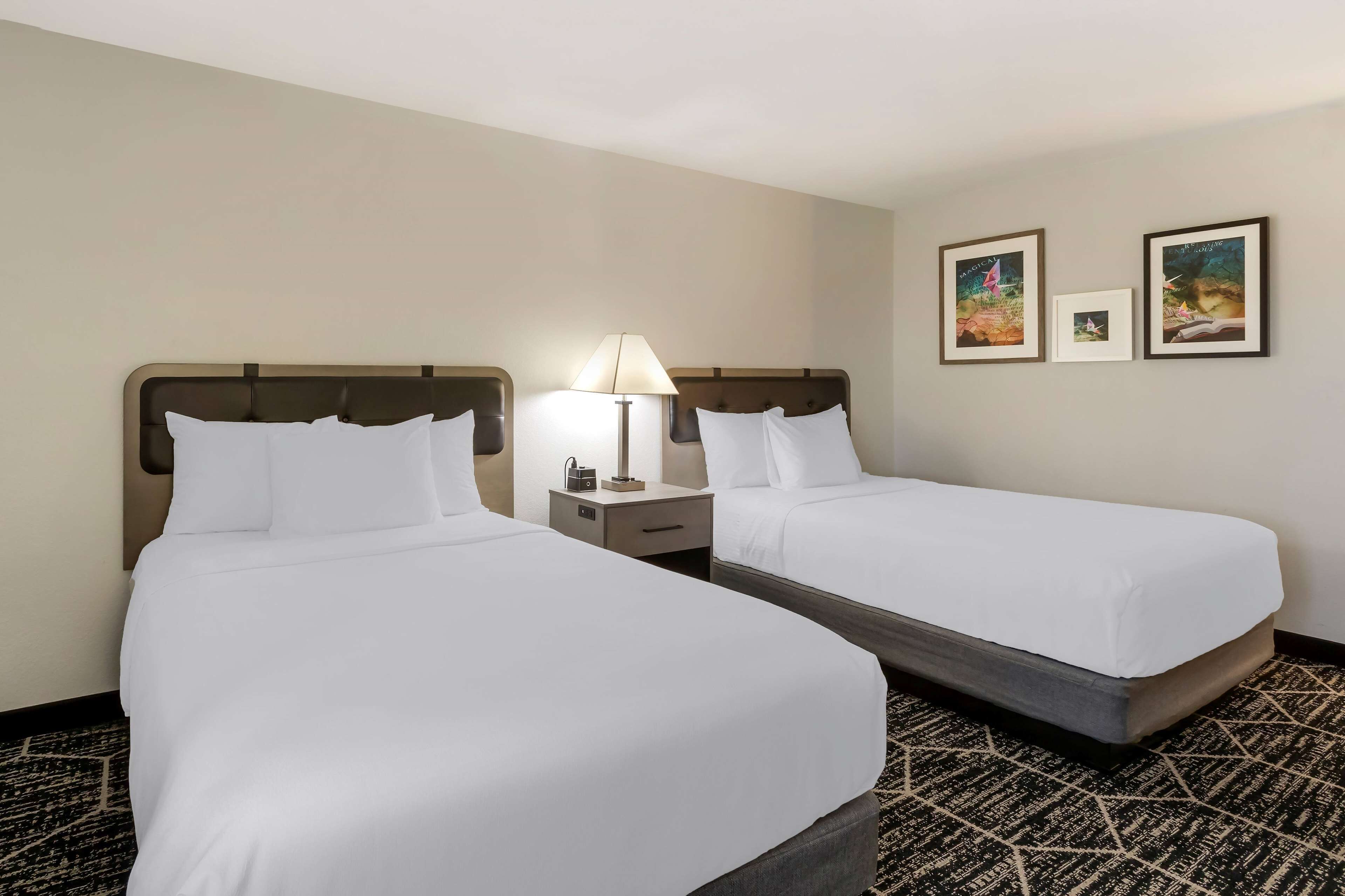 A hotel room with two beds, a nightstand with a lamp, and two framed pictures on the wall.
