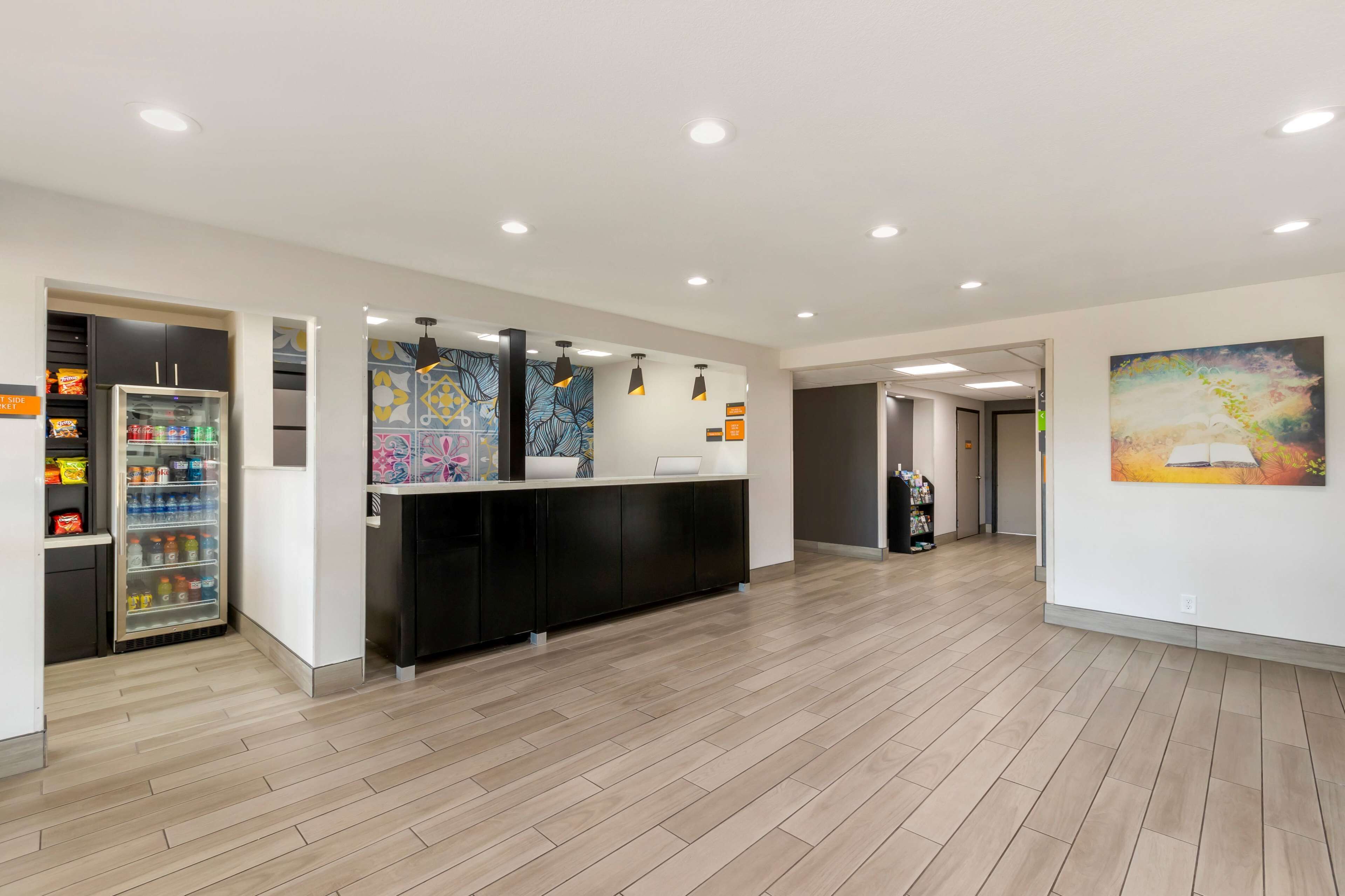 A modern reception area with a counter, a refrigerator stocked with beverages, and a colorful abstract painting on the wall.