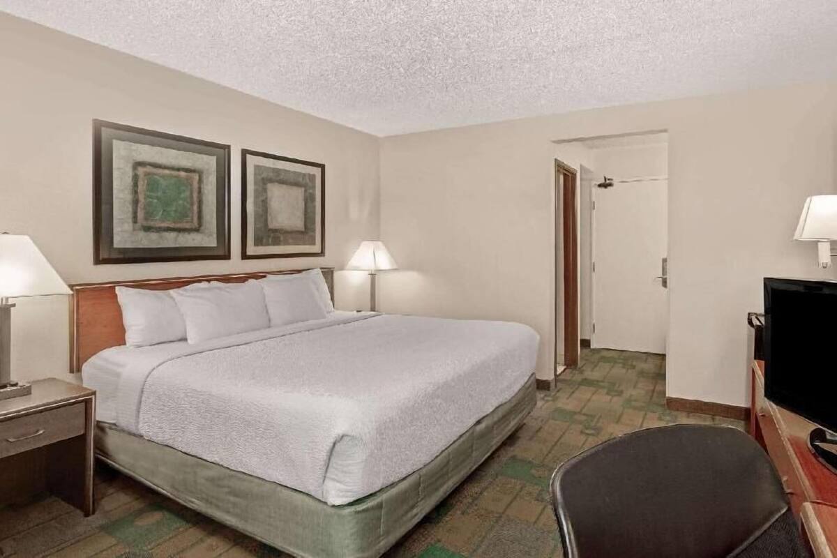 A hotel room with a bed, two bedside lamps, a television, and a door leading to another room.