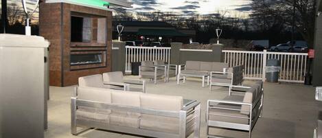 An outdoor seating area with modern furniture, a barbecue grill, and a building with a green awning.