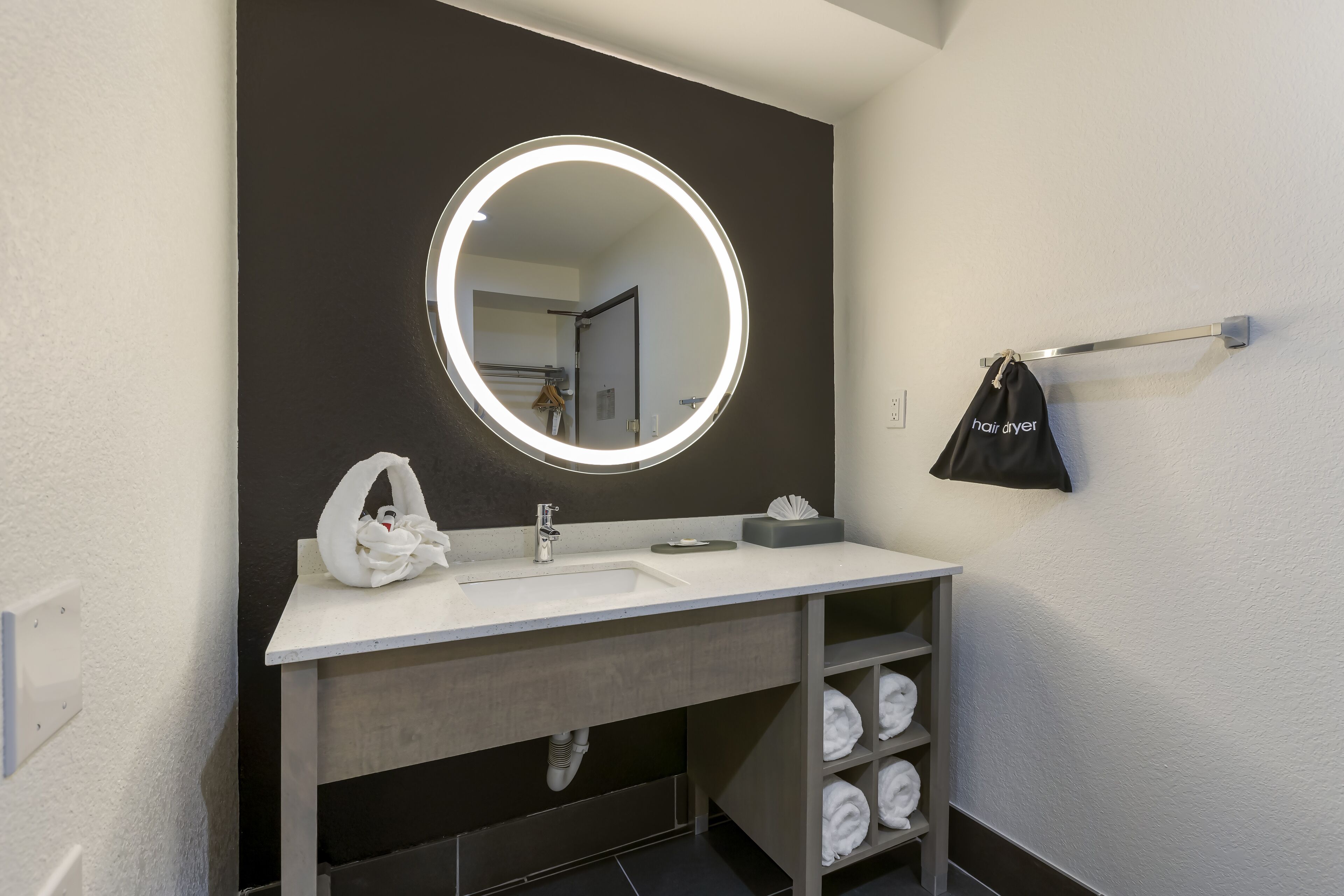 Een moderne badkamer met een ronde spiegel, een witte wastafel en een handdoekhouder.