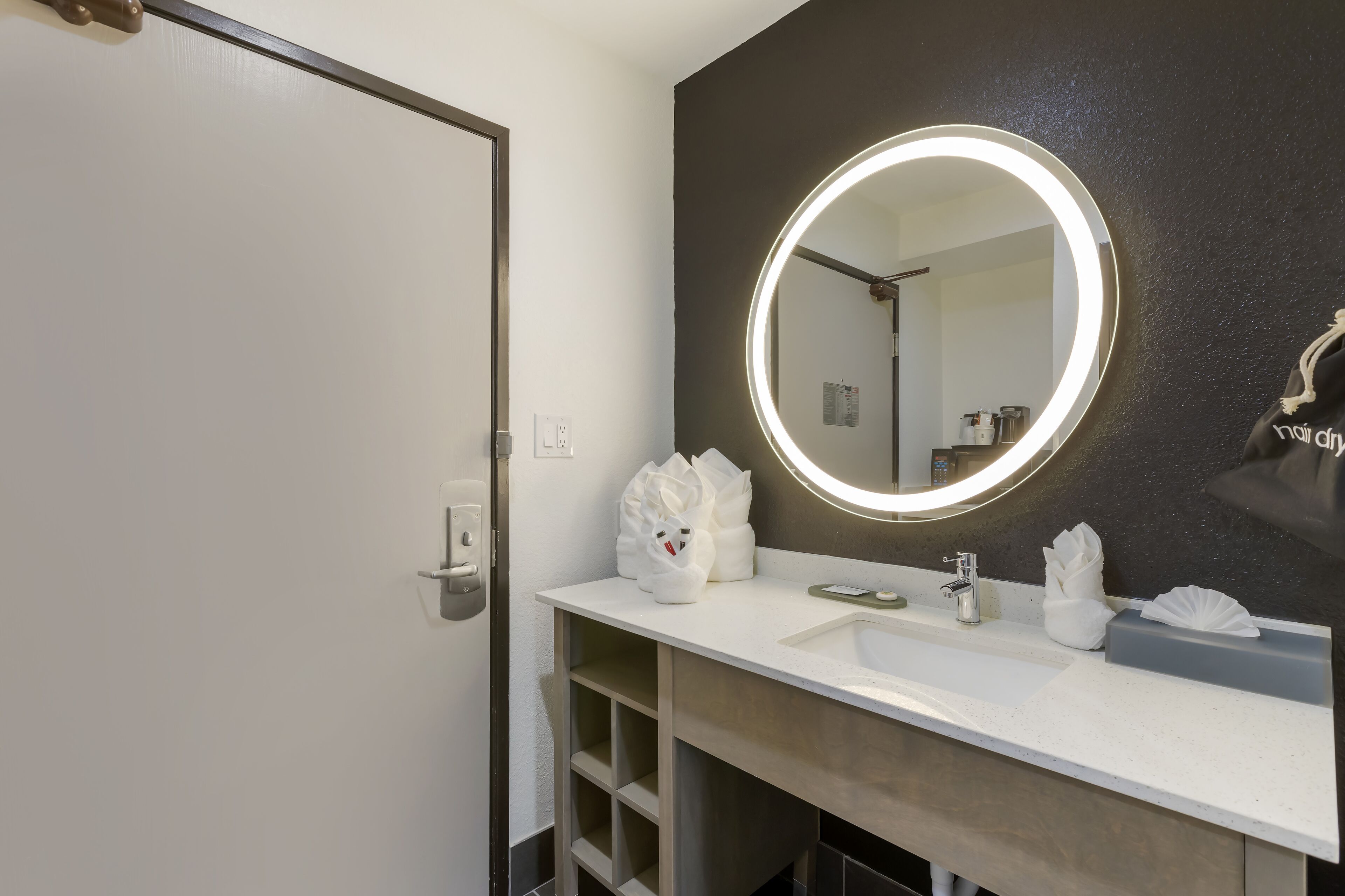 A bathroom with a white sink, a round mirror with a light, and a towel rack.