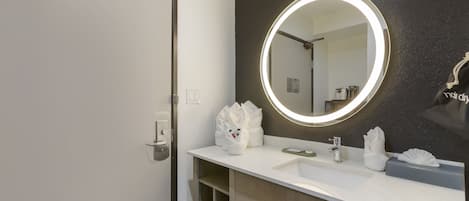 A bathroom with a white sink, a round mirror with a light, and a towel rack.