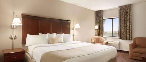Habitación de hotel con una cama grande, dos lámparas fijadas a la pared, un ventilador de techo, una ventana con cortinas y una silla.
