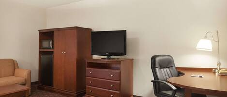 A hotel room with a wooden cabinet, a television, a desk with a lamp, a chair, and a patterned carpet.