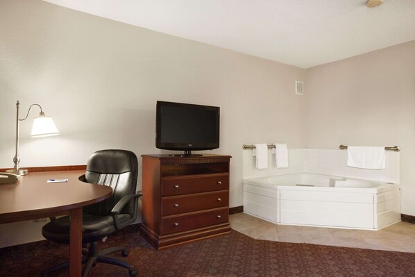 Habitación de hotel con escritorio, silla, televisor y una bañera grande.